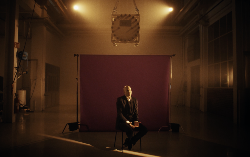 Nel CEO Håkon Volldal sitting in front of a backdrop in an empty storage warehouse in dimmed lighting with a spotlight on him